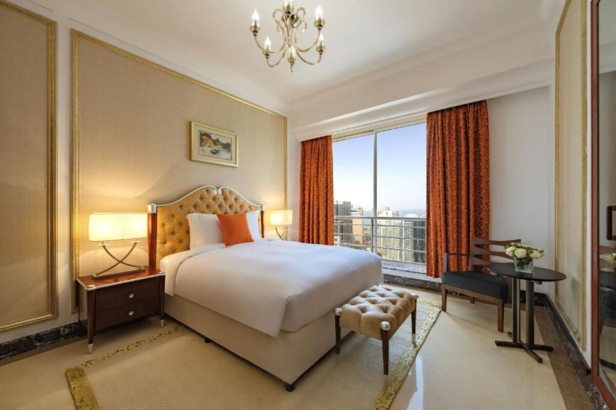 A hotel room with a large bed, a desk, a chair, and a view of the city.