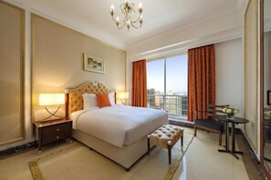 A hotel room with a large bed, a desk, a chair, and a view of the city. - Dusit Hotel and Suites Doha (Doha)