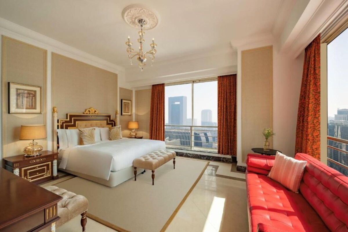 A hotel room with a large bed, a red sofa, a chandelier, and a view of the city.