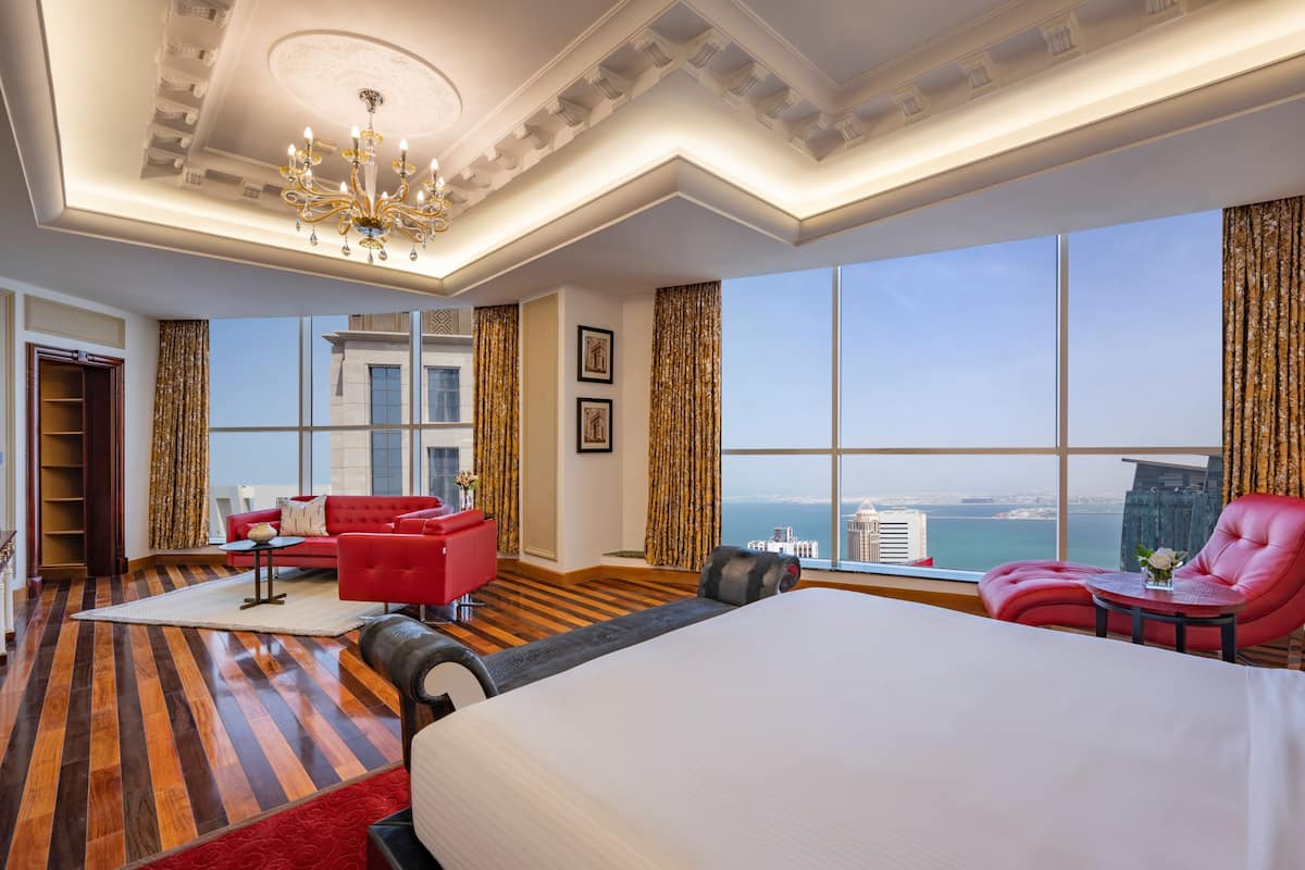 Ein Hotelzimmer mit einem großen Bett, einem roten Sofa, einem roten Sessel, einem kleinen Tisch und Blick auf die Stadt.