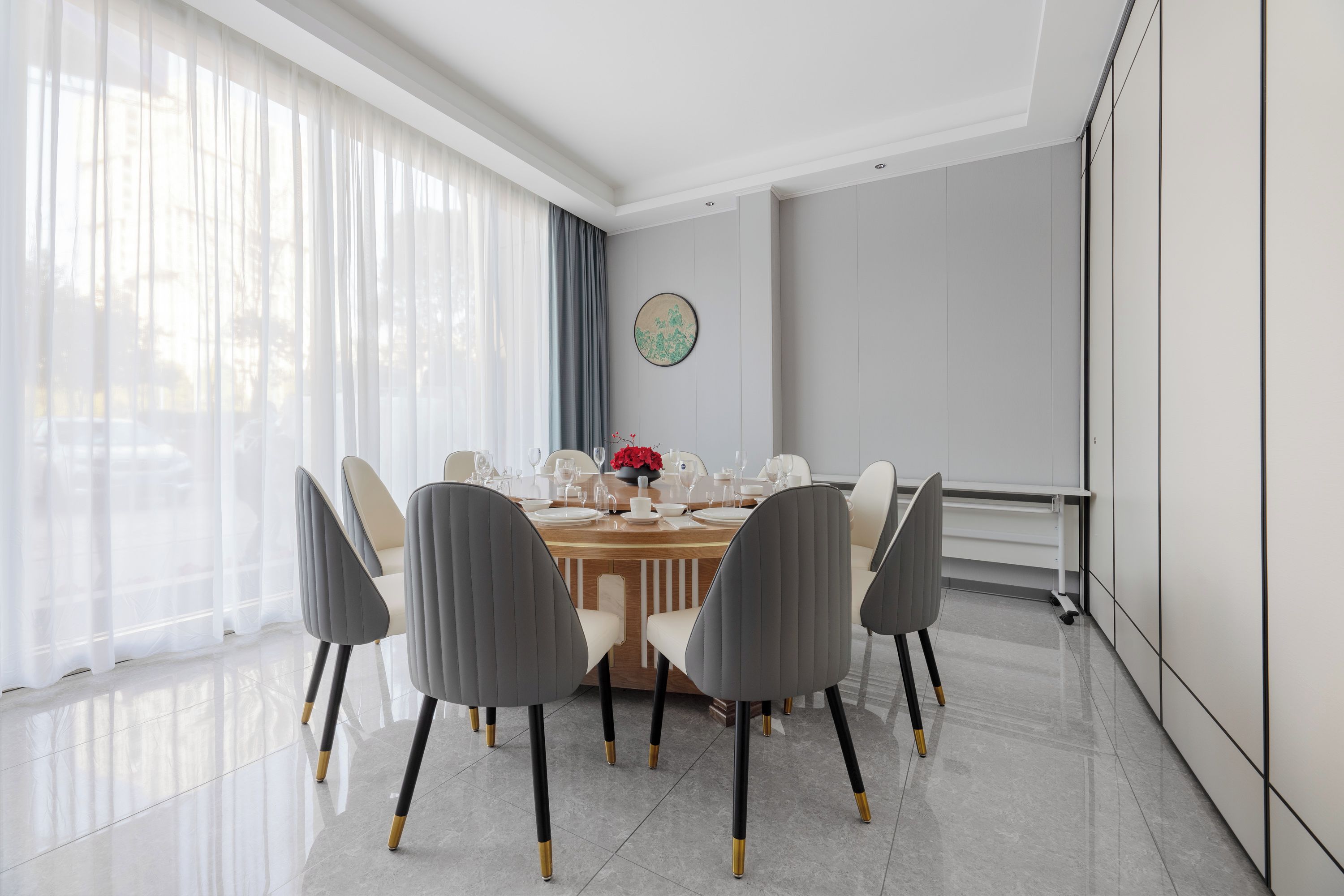 Un comedor moderno con una mesa redonda, seis sillas y un florero con flores rojas.