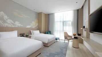 Habitación de hotel con dos camas, un escritorio, un televisor y un ventanal con cortinas.