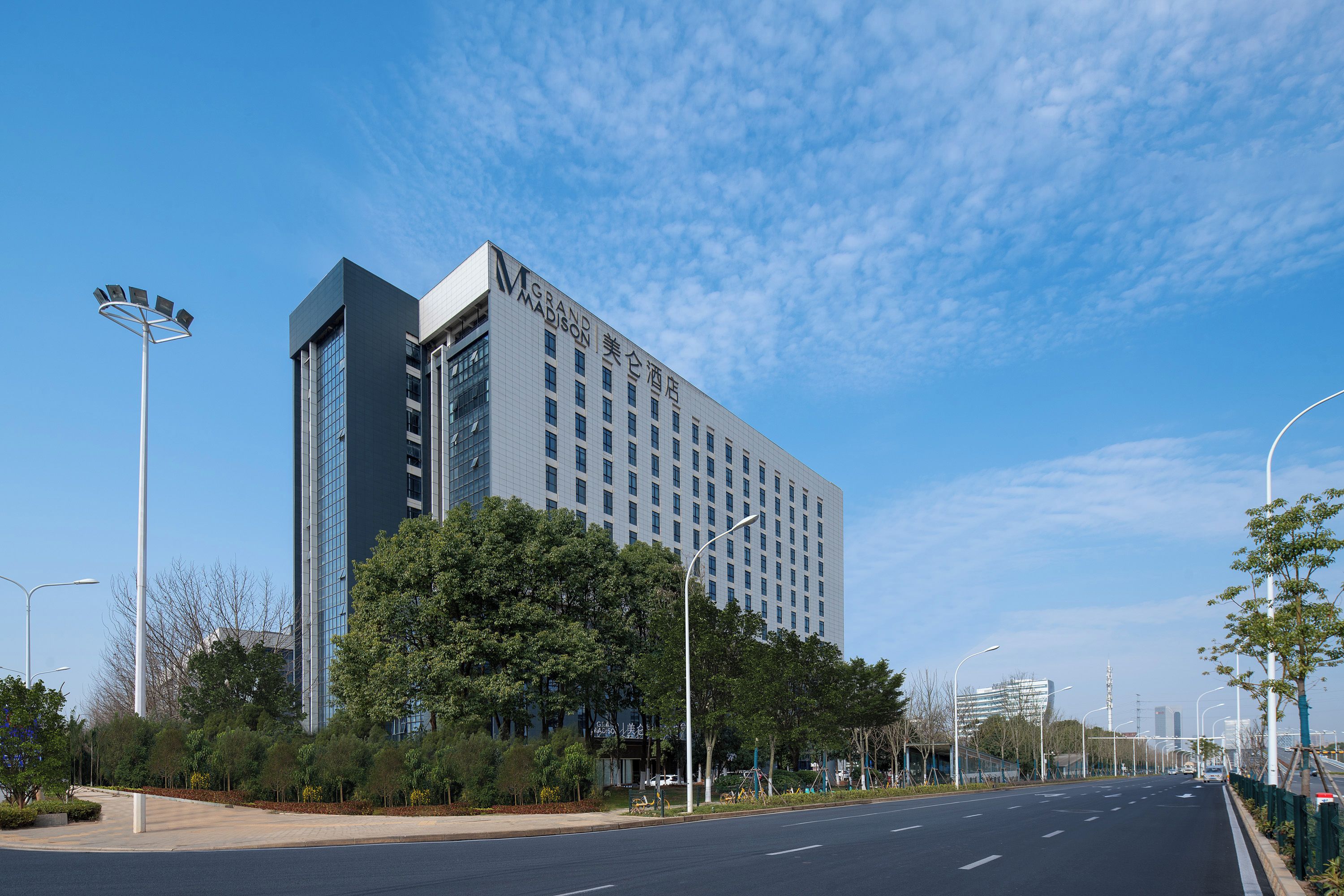 A modern hotel with a prominent 'GRAND MADISON' sign, surrounded by greenery and a clear sky.