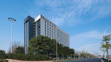 A modern hotel with a prominent 'GRAND MADISON' sign, surrounded by greenery and a clear sky.