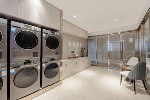 Een wasserette met meerdere wasmachines, een klein tafeltje met een vaas, en een stoel.