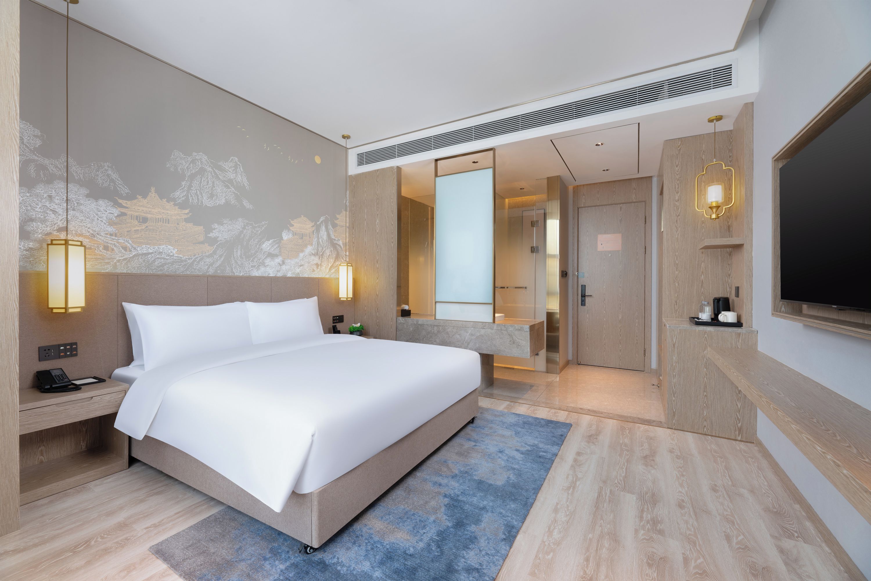 A modern hotel room with a large bed, bedside lamps, a flat-screen TV, and a bathroom visible through an open door.
