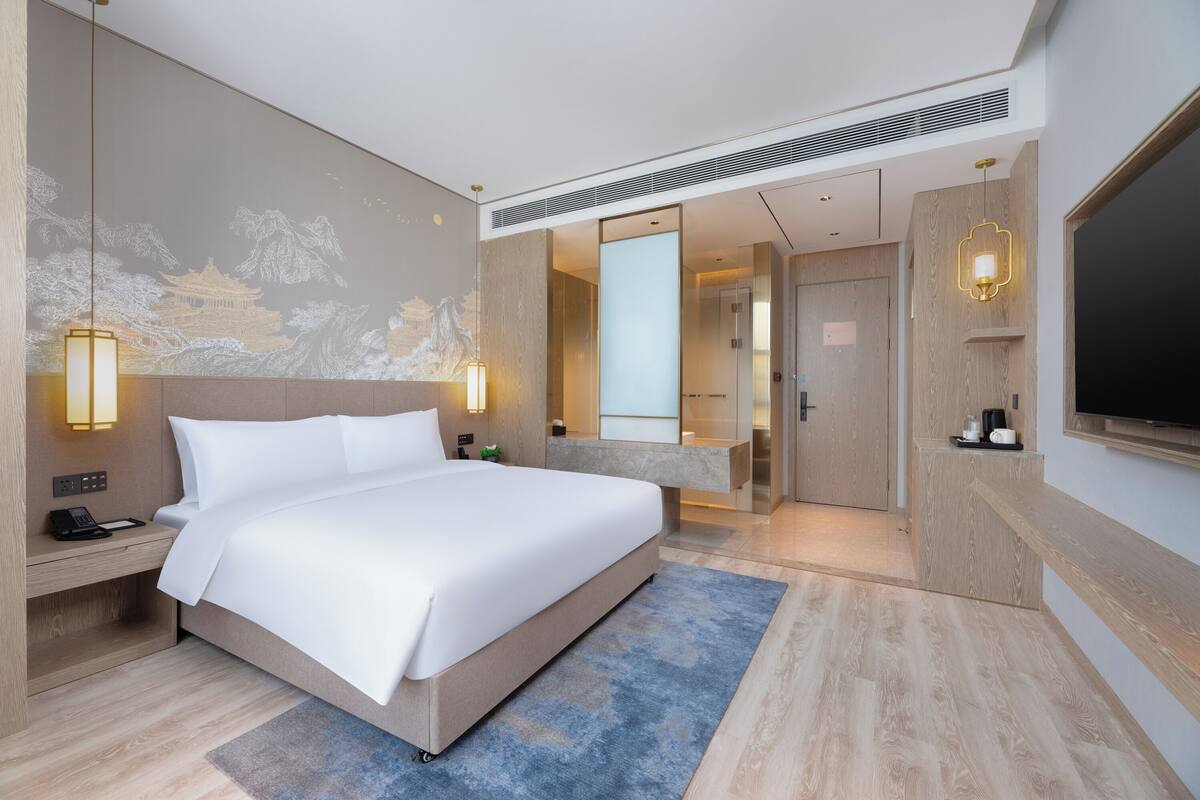 Ein modernes Hotelzimmer mit einem großen Bett, Nachttischlampen, einem Flachbildfernseher und einem durch eine geöffnete Tür einsehbaren Badezimmer.