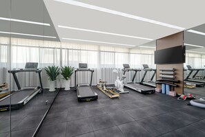 Une salle de sport moderne équipée de plusieurs tapis de course, de vélos d’appartement et d’un rameur.