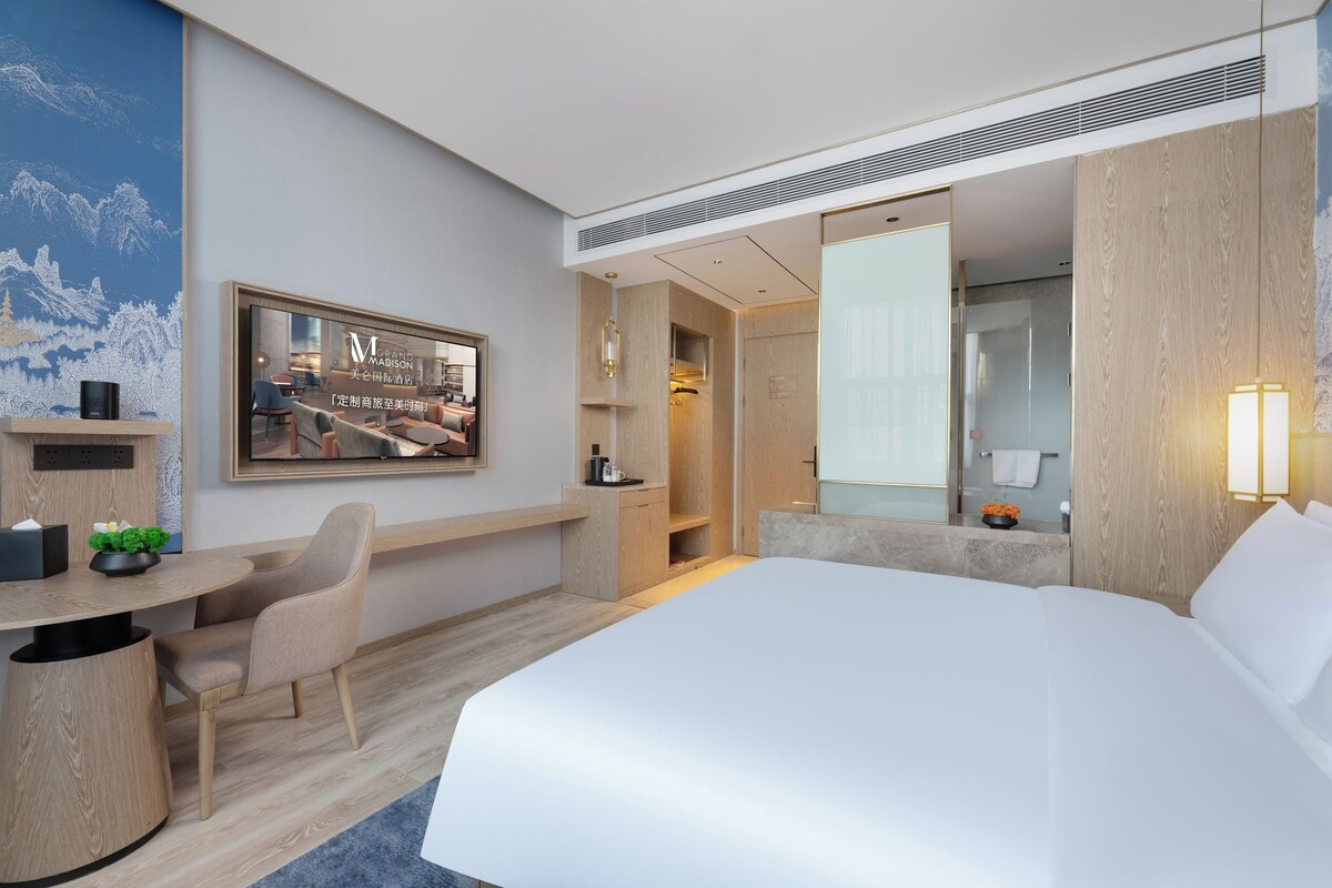 Une chambre d’hôtel équipée d’un lit, d’un bureau, d’une chaise, d’un miroir et d’un téléviseur fixé au mur.