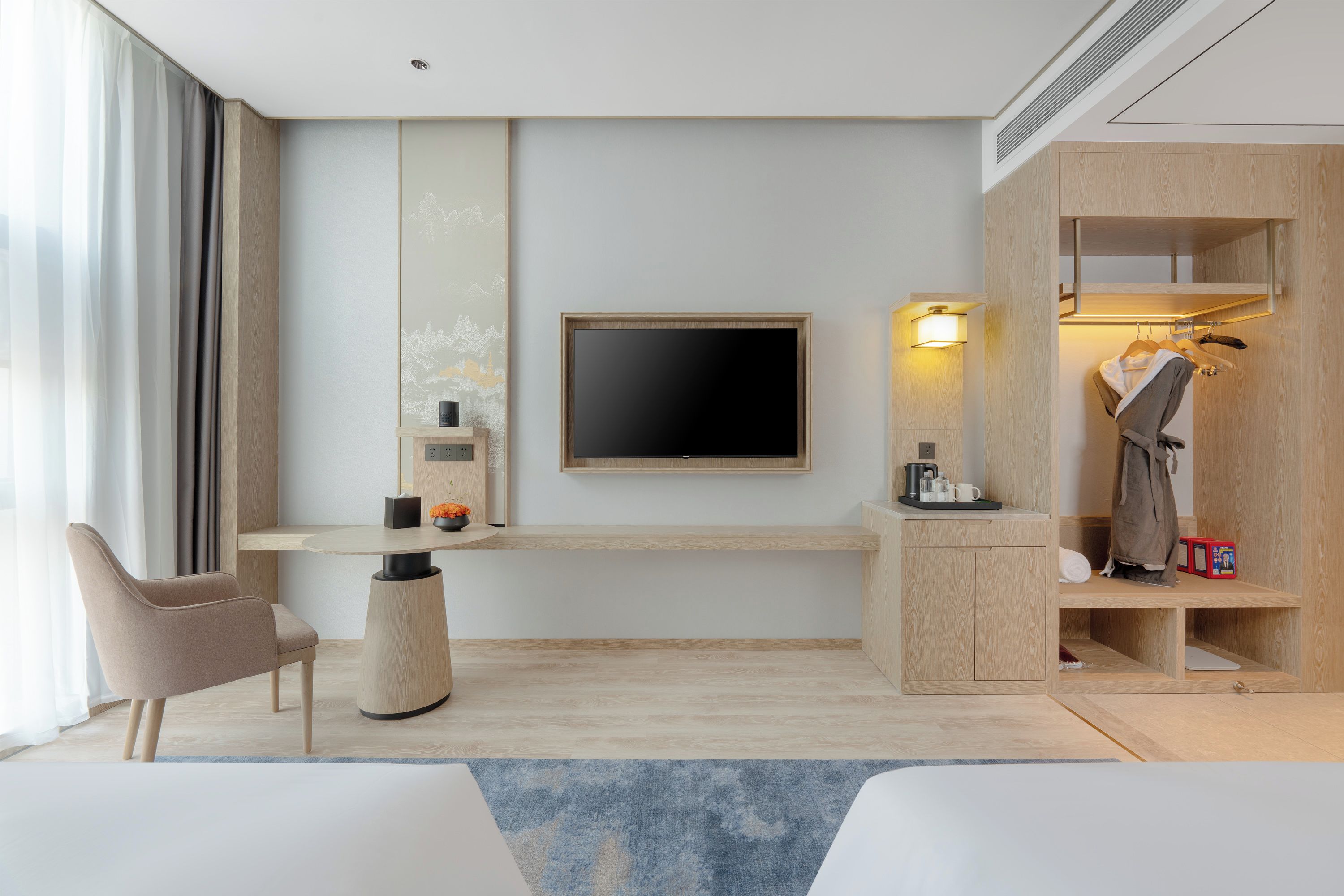 A modern hotel room with a flat-screen TV, a desk with a chair, a coat rack, and a bed.