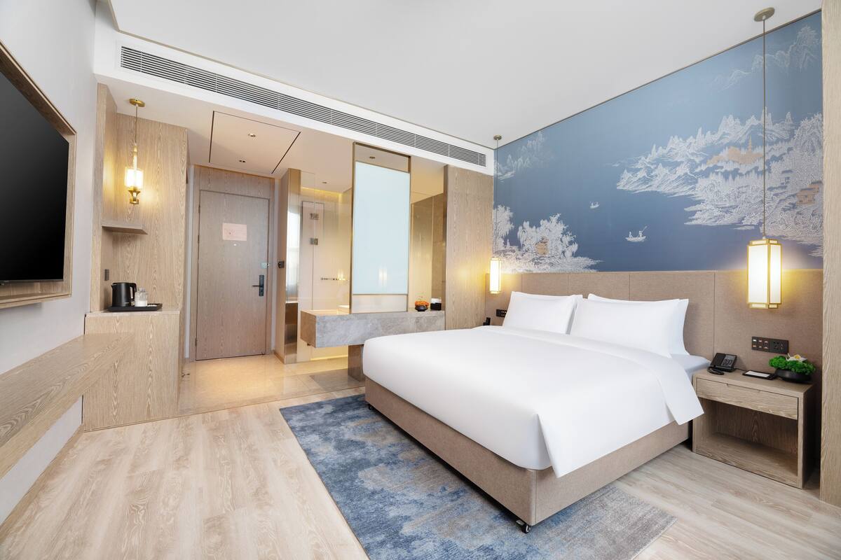 Ein modernes Hotelzimmer mit einem großen Bett, einem Flachbildfernseher, einem Badezimmer und einem Wandbild.