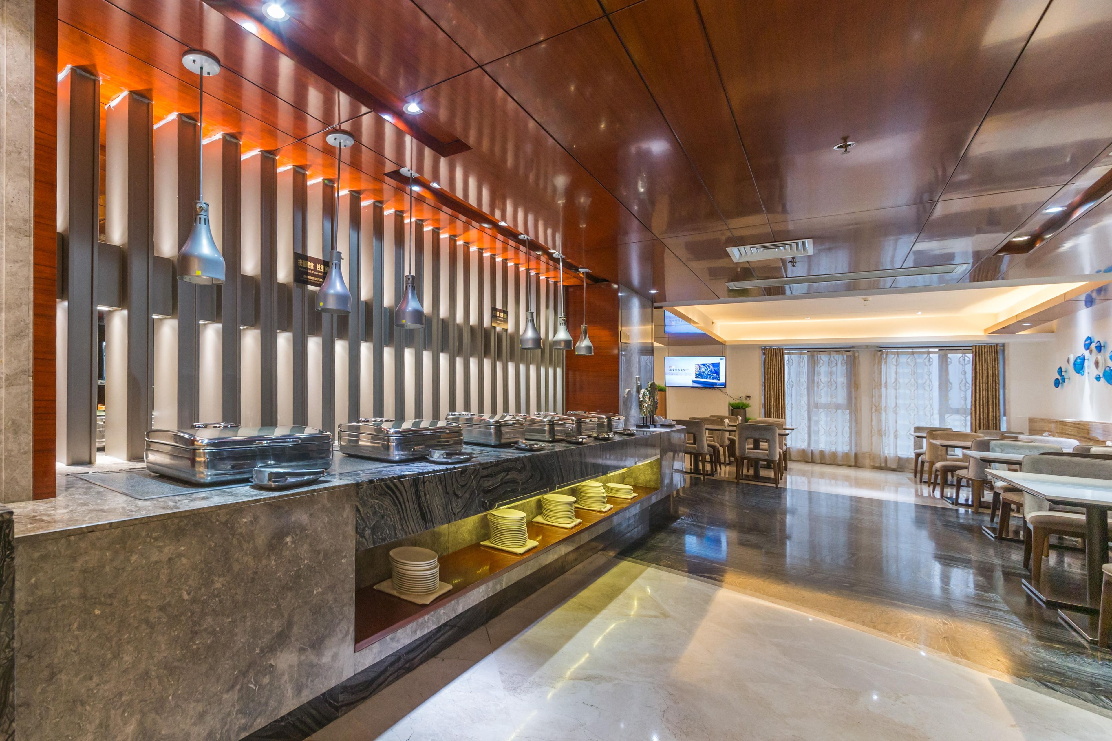 Un moderno vestíbulo de hotel con un mostrador de recepción de mármol, una zona de buffet y un área de descanso con mesas y sillas.