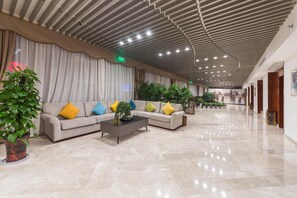 A spacious lobby with a modern ceiling design, a sectional sofa with colorful cushions, and potted plants.
