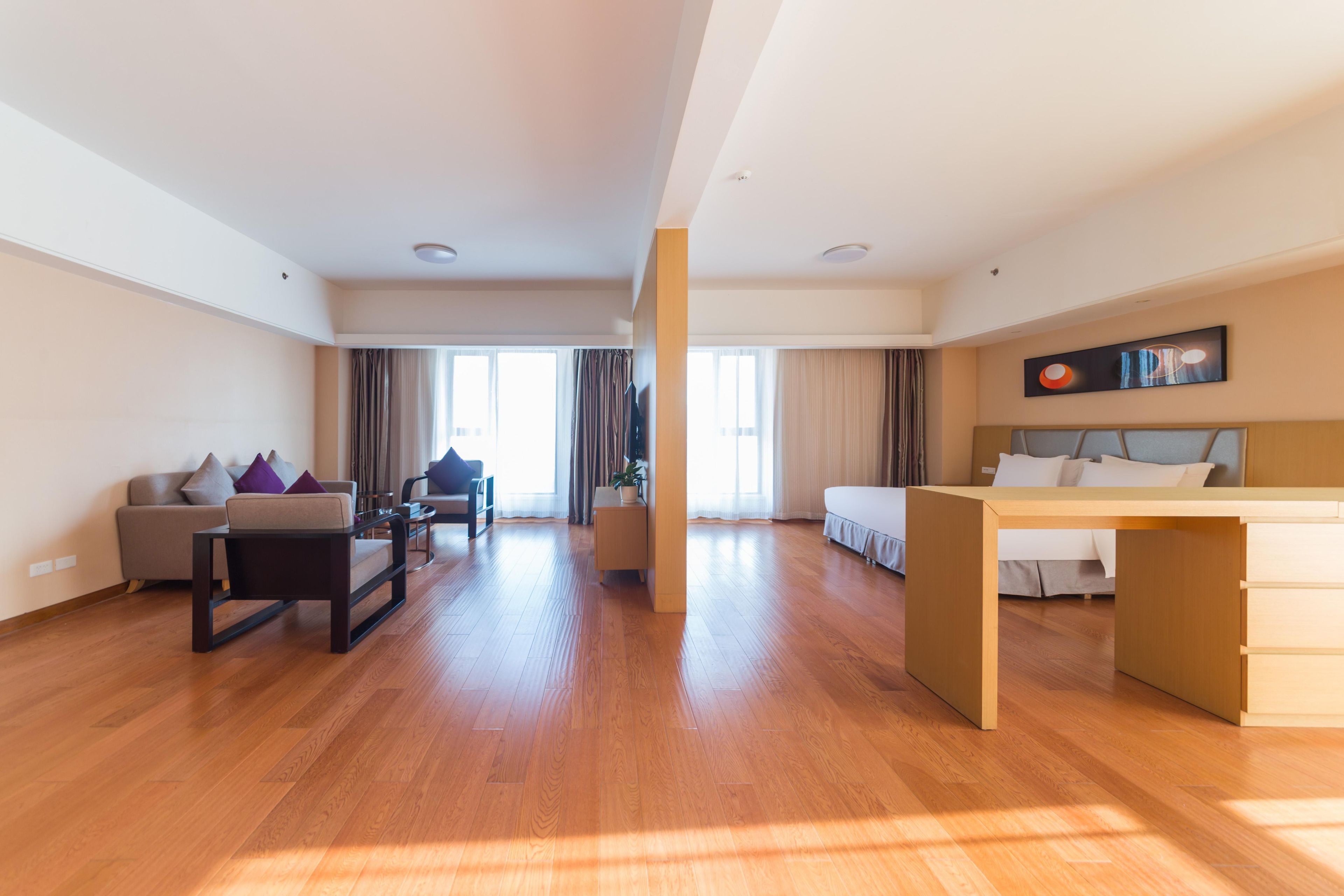 Una habitación de hotel moderna con suelo de madera, un sofá, un escritorio, una cama y un ventanal grande.