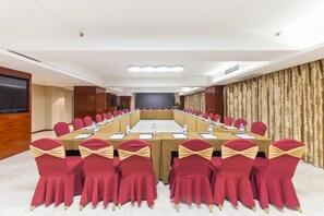 Un salón de conferencias con una larga mesa, sillas rojas con fajas doradas y una pantalla grande.