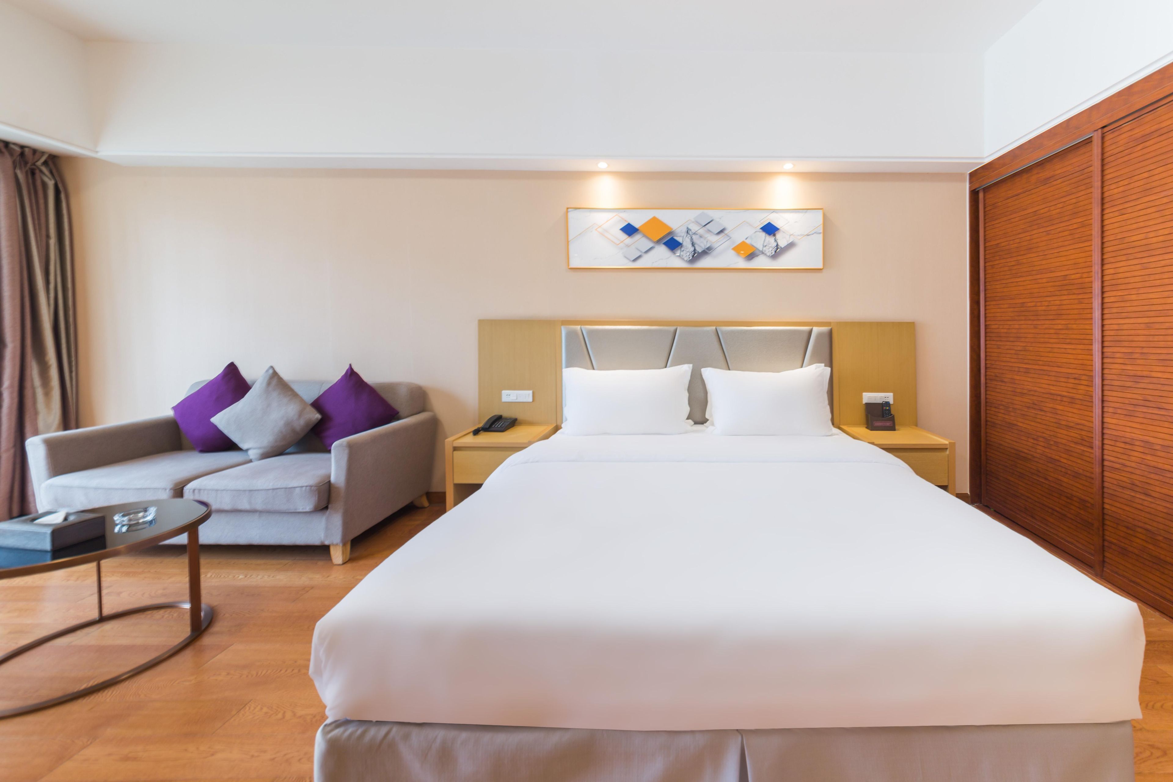 A hotel room with a large bed, a sofa, a bedside table, a nightstand, and a wooden wardrobe.
