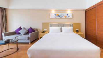 A hotel room with a large bed, a sofa, a bedside table, a nightstand, and a wooden wardrobe.