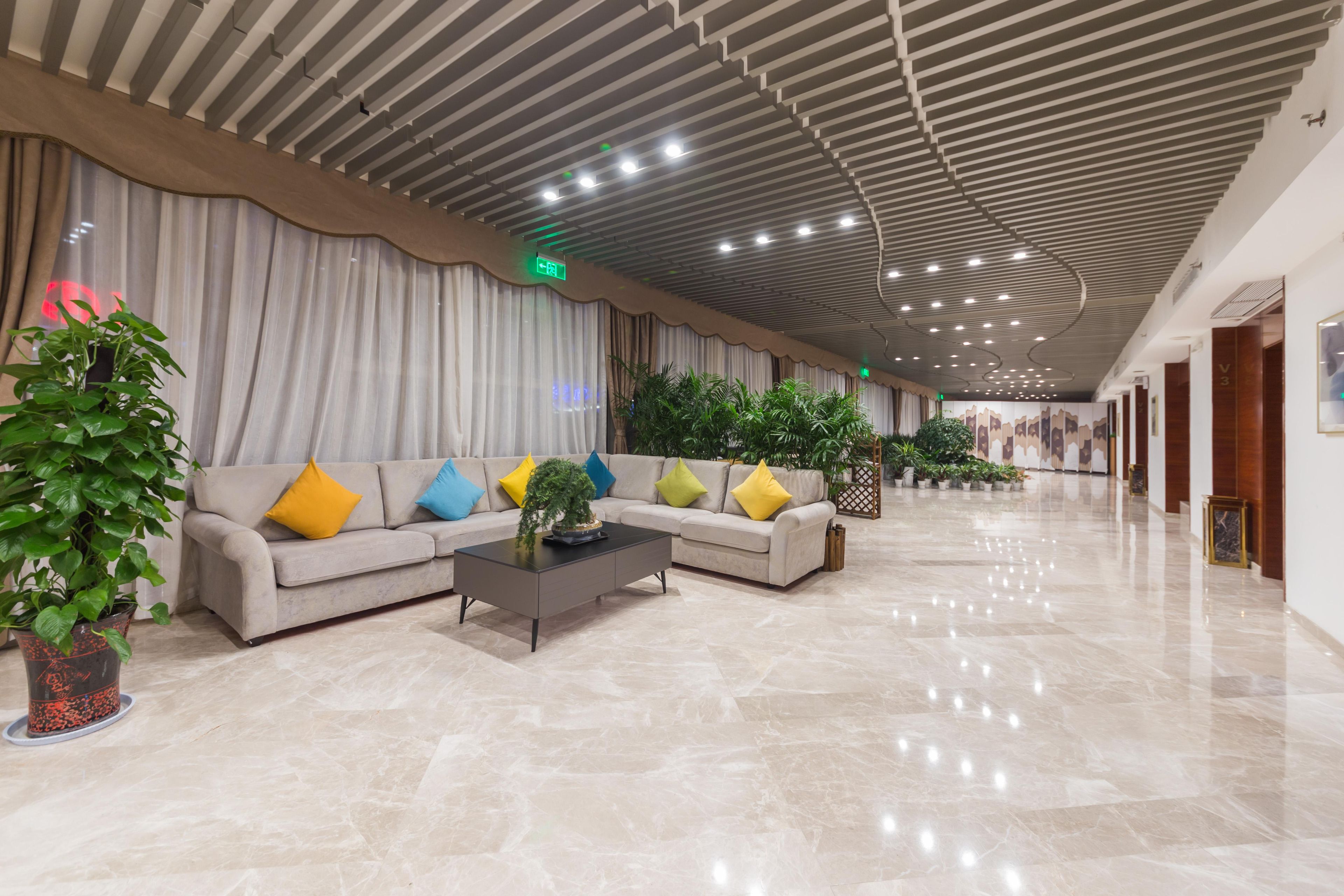 Eine großzügige Lobby mit modernem Deckenstil, einem Ecksofa mit bunten Kissen und Topfpflanzen.