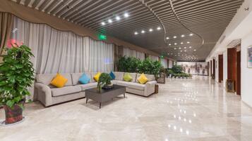 Eine großzügige Lobby mit modernem Deckenstil, einem Ecksofa mit bunten Kissen und Topfpflanzen.