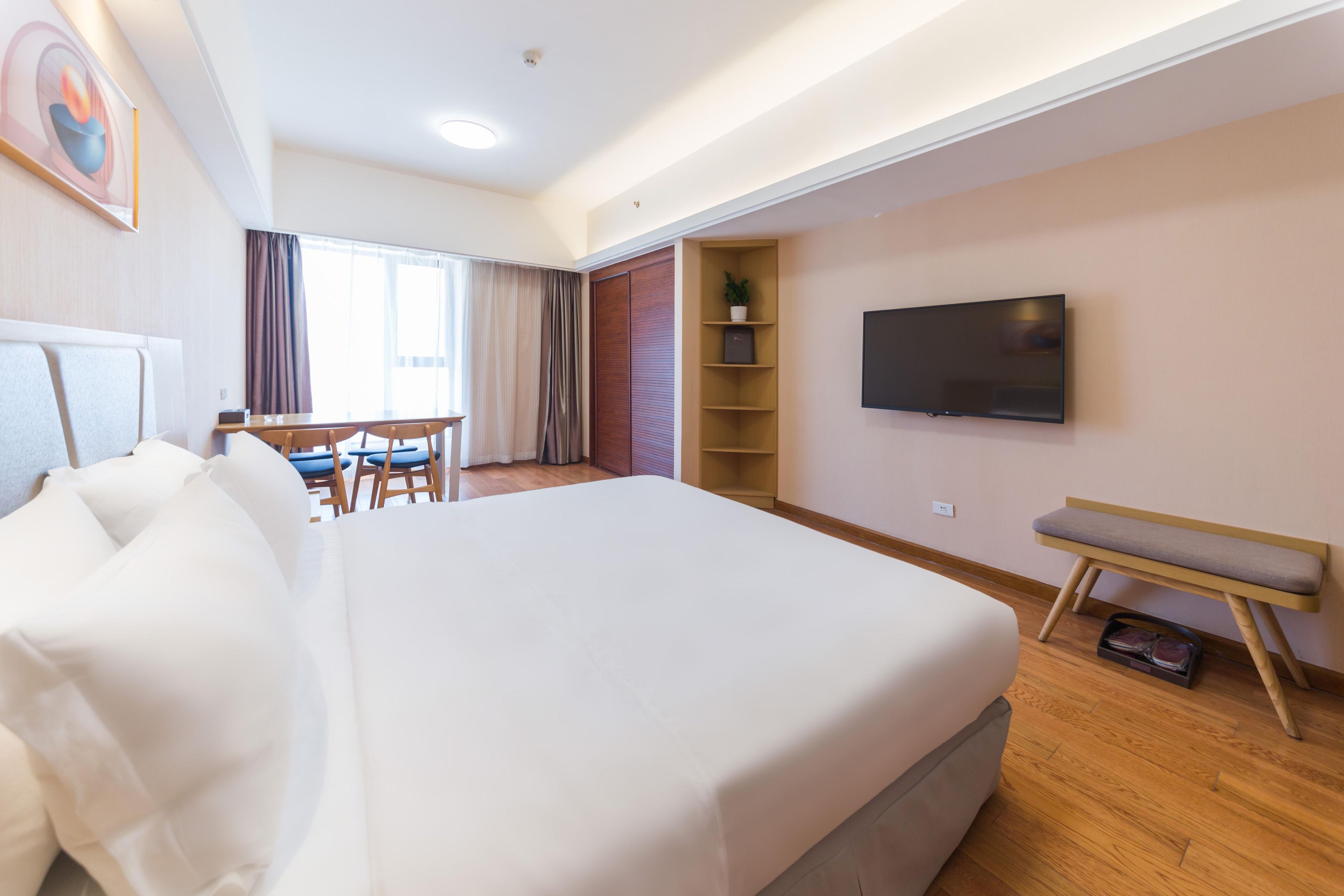 Habitación de hotel con una cama grande, un escritorio, una silla, un televisor y una estantería con una planta.