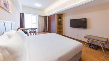 Habitación de hotel con una cama grande, un escritorio, una silla, un televisor y una estantería con una planta.