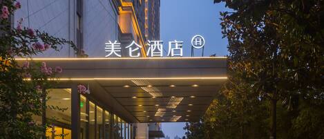 A hotel entrance with a covered walkway, glass doors, and a sign with Chinese characters.