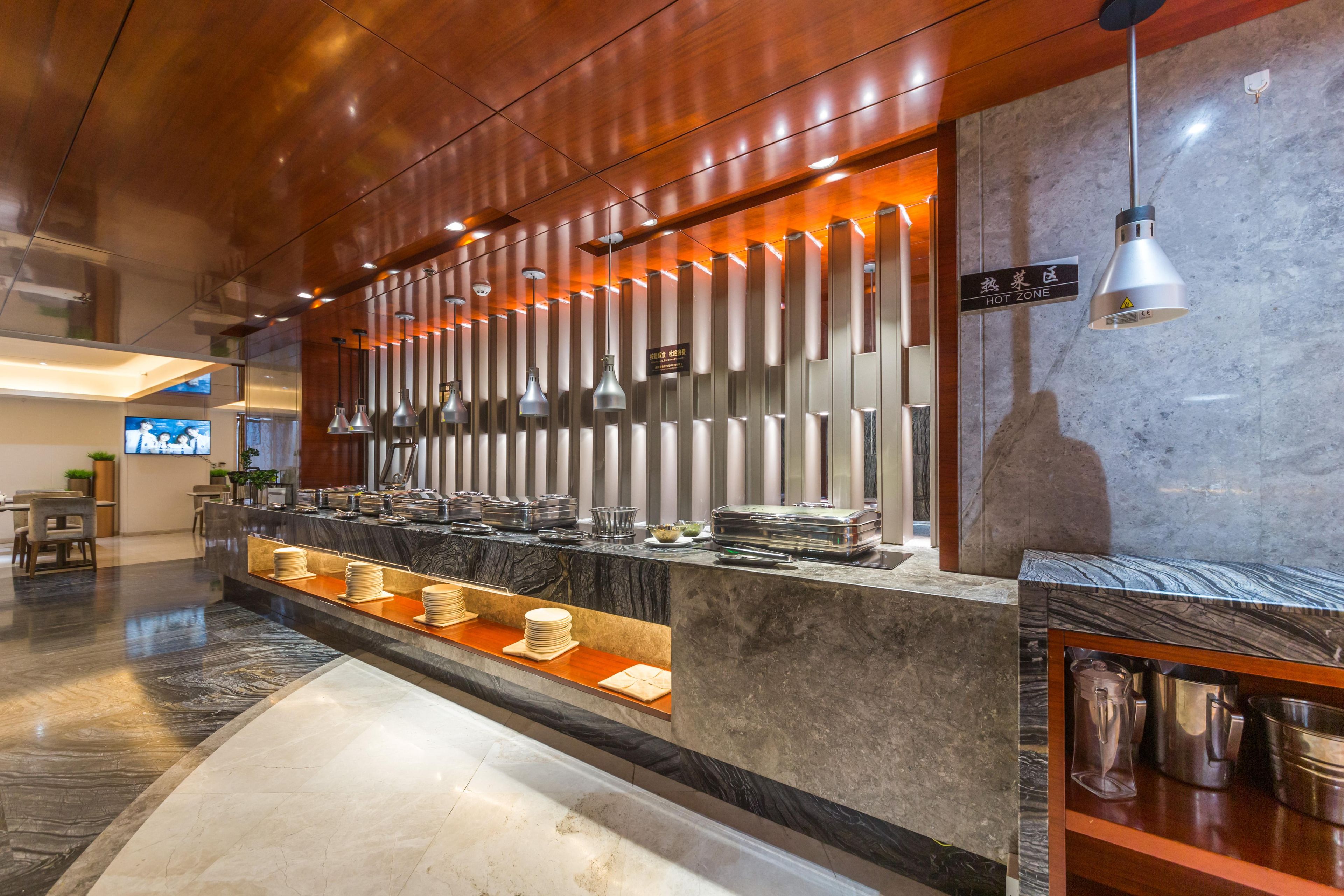 Zona de buffet con mostrador de mármol, iluminación colgante y señalización de 'ZONA CALIENTE'.
