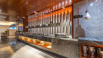 Zona de buffet con mostrador de mármol, iluminación colgante y señalización de 'ZONA CALIENTE'.
