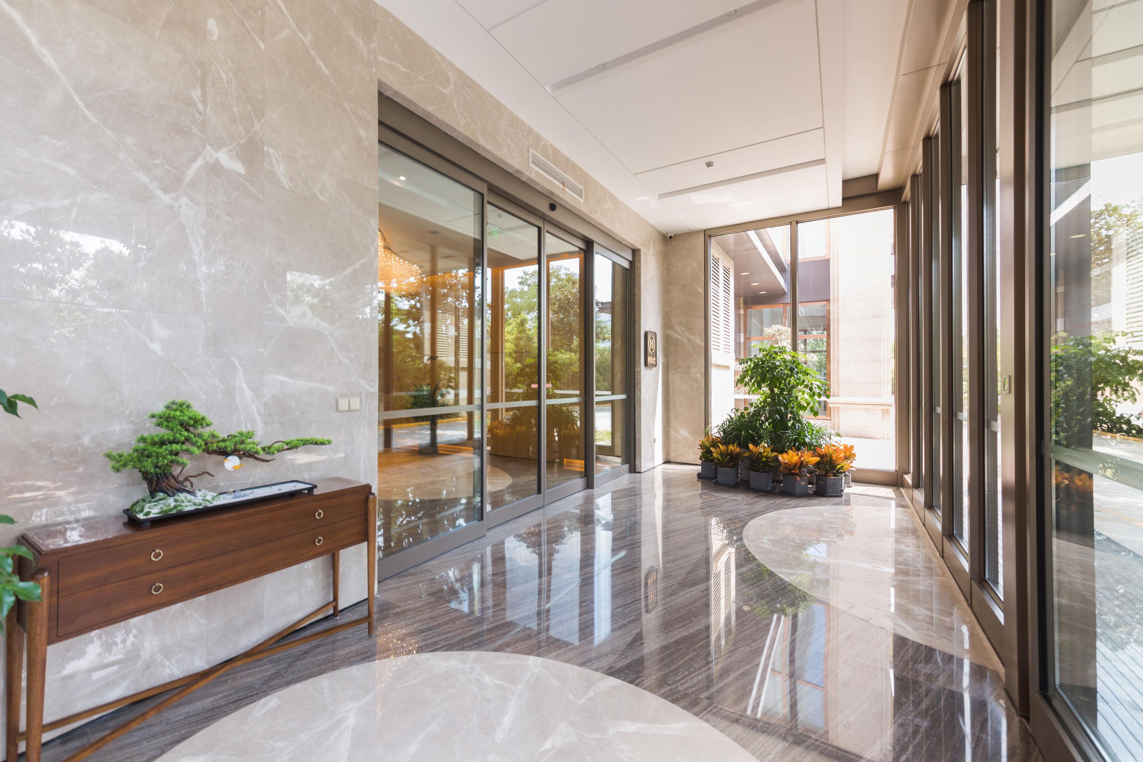 A modern lobby with a marble floor, a wooden bench, glass doors, and potted plants.
