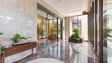 A modern lobby with a marble floor, a wooden bench, glass doors, and potted plants.