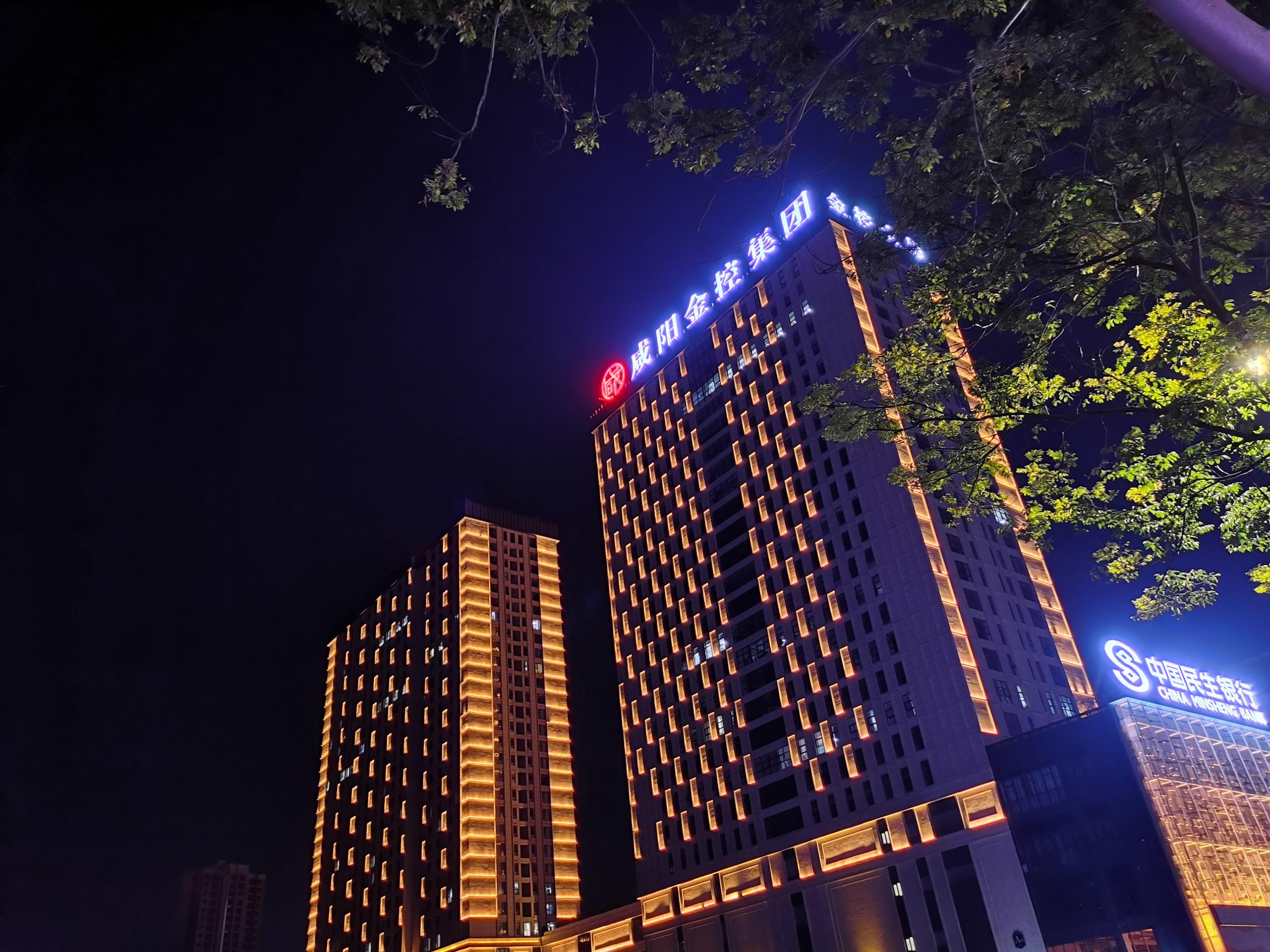 Dos edificios de gran altura con señalización iluminada, uno con un logotipo circular rojo y el otro con uno azul.