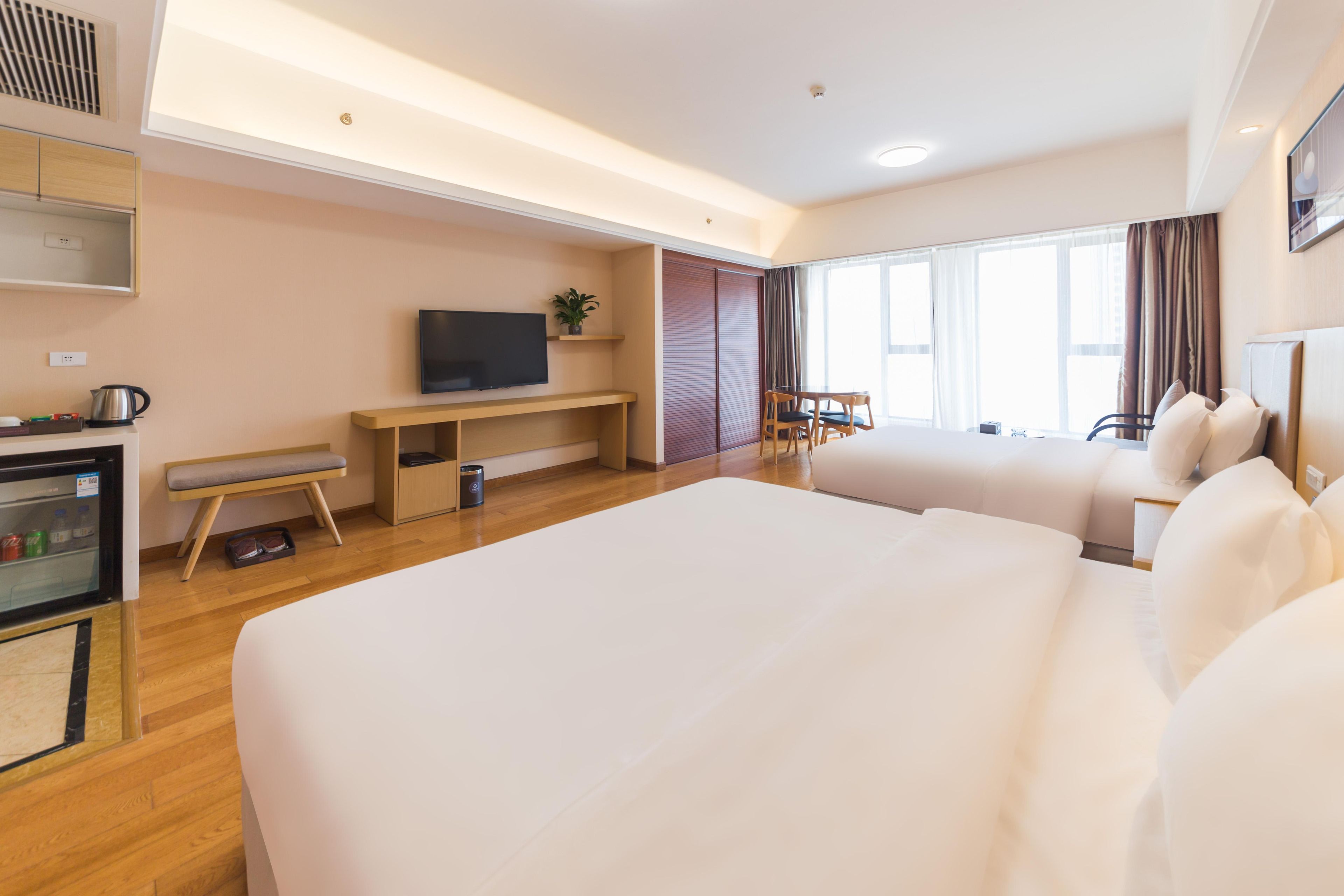 A hotel room with a large bed, a TV, a desk, a chair, a small table, and a window with curtains.