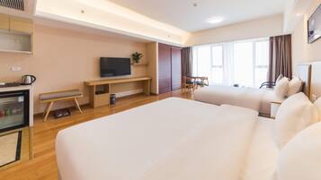 Ein Hotelzimmer mit einem großen Bett, einem Fernseher, einem Schreibtisch, einem Stuhl, einem kleinen Tisch und einem Vorhangfenster.