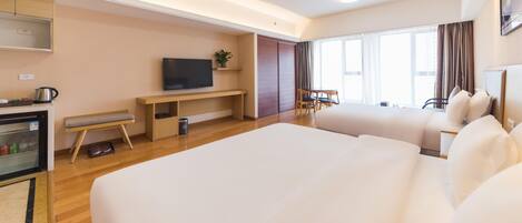 A hotel room with a large bed, a TV, a desk, a chair, a small table, and a window with curtains.