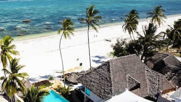 Un resort sulla spiaggia con piscina, palme e vista sull'oceano.