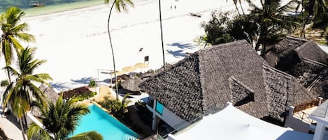 A beach resort with a pool, palm trees, and a view of the ocean.