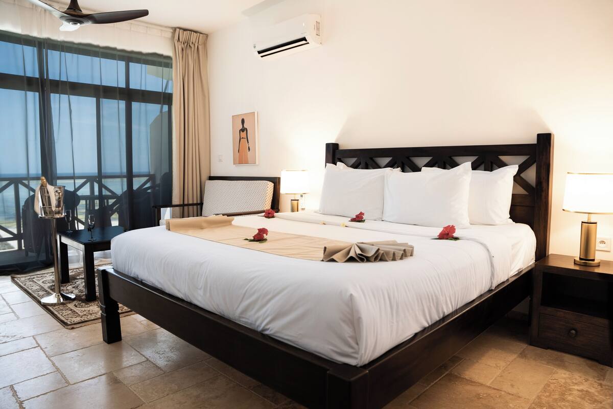 Una habitació d'hotel amb un llit gran, una tauleta de nit i una finestra amb cortines que dona a l'exterior.