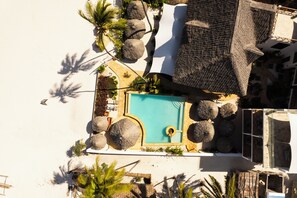 Vista aérea de un complejo turístico con piscina, sillones de descanso y construcciones de techo de paja.