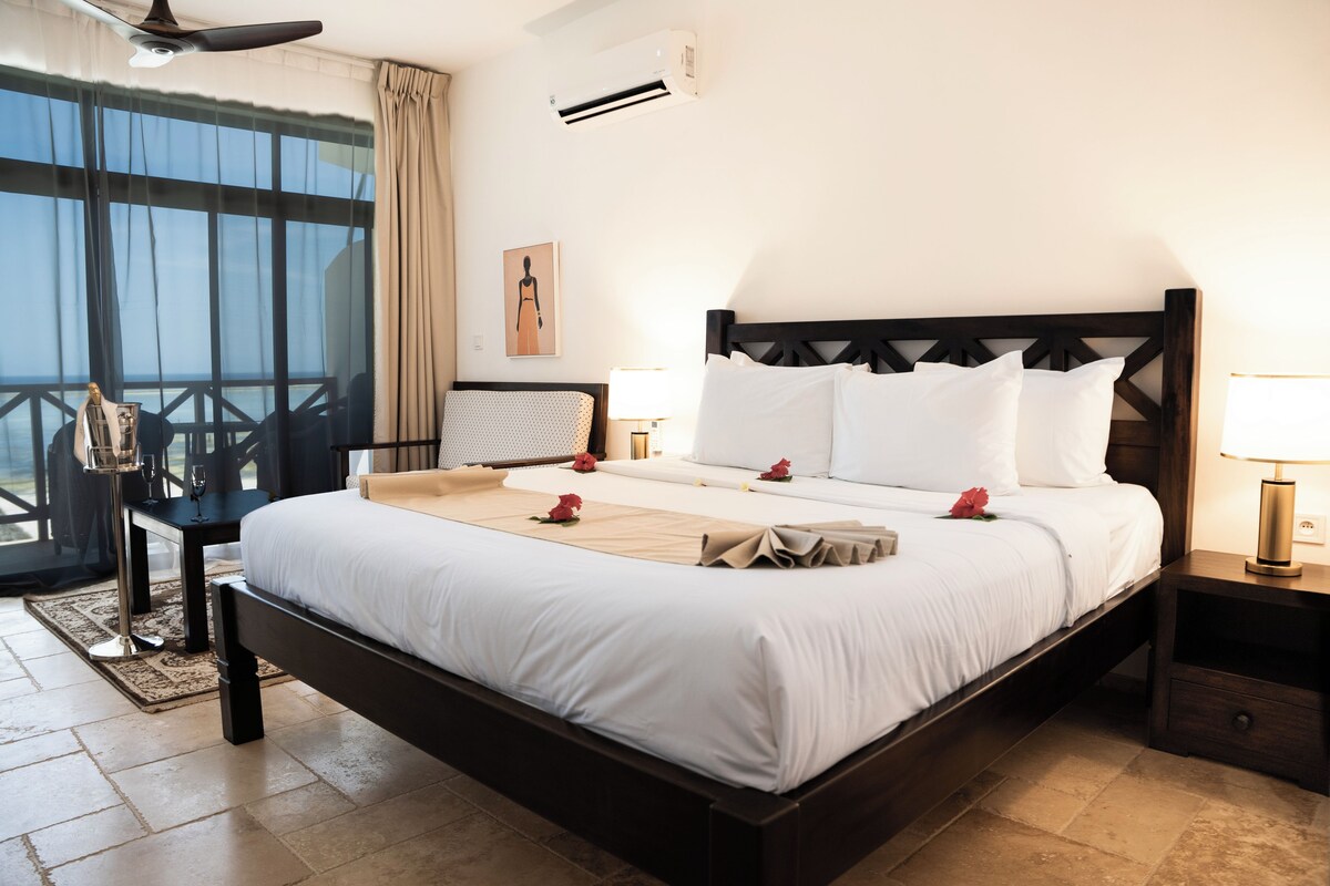 Habitación de hotel con una cama grande, una mesita de noche y cortinas en la ventana, con vista al exterior.