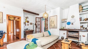 A living room with a sofa, a wooden table, a hanging light fixture, and a fireplace. - Lu Maggiu, Santa Teresa di Gallura, Italy (Santa Teresa di Gallura)