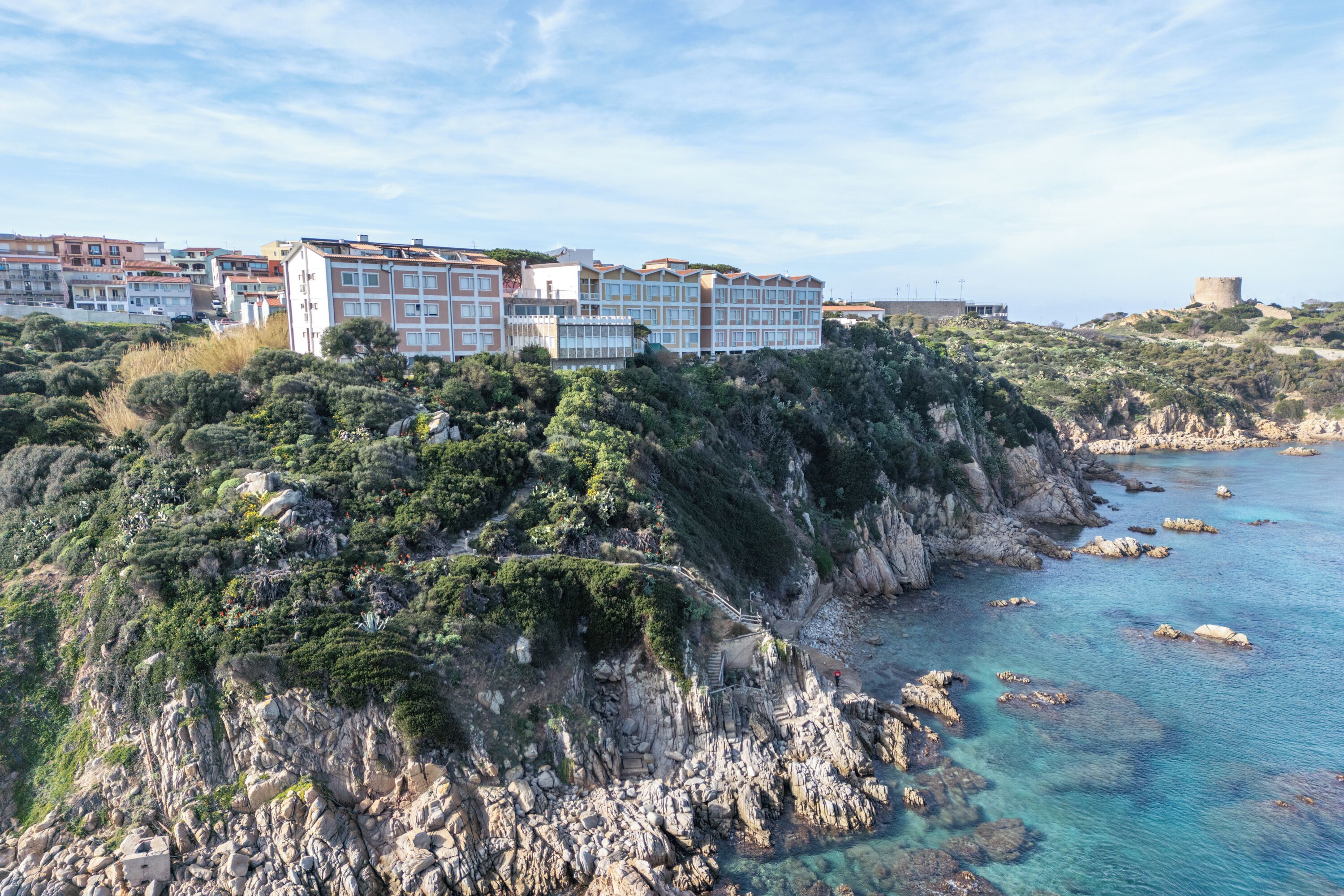 A coastal hotel with multiple buildings, rocky cliffs, and clear blue waters.