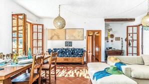 A dining area with a wooden table and chairs, a sofa, and a hanging light fixture. - Lu Maggiu, Santa Teresa di Gallura, Italy (Santa Teresa di Gallura)