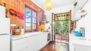 A kitchen with a brick backsplash, white cabinetry, a stove, and a hanging light fixture. - Lu Maggiu, Santa Teresa di Gallura, Italy (Santa Teresa di Gallura)