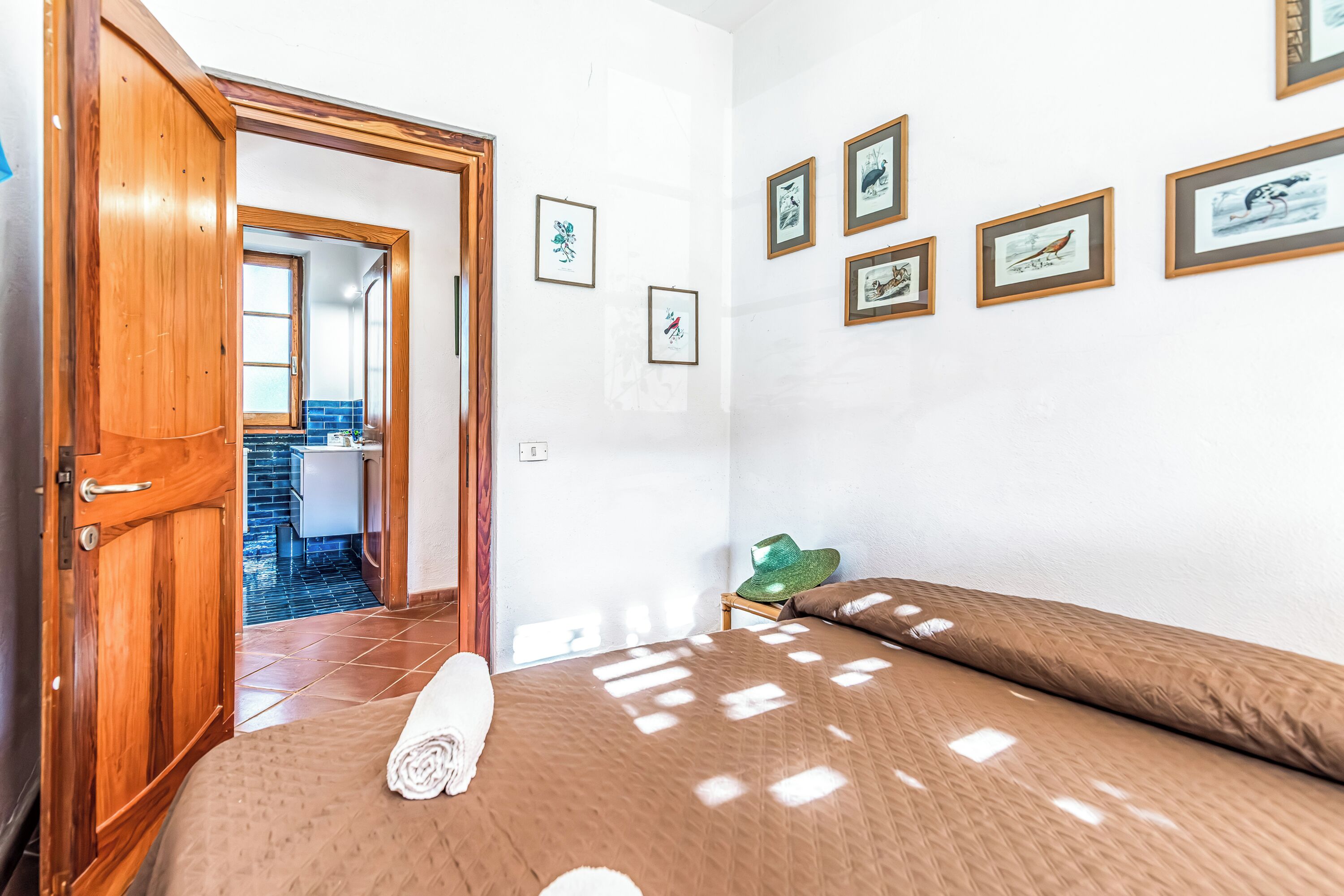 Ein Zimmer mit einem Bett, einer Holztür, einem grünen Hut auf einem Stuhl und gerahmten Bildern an der Wand.
