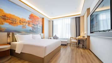 A modern hotel room with a large bed, a desk, a chair, a TV, and a painting of autumn trees.