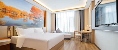 Quarto de hotel moderno com uma cama grande, uma escrivaninha, uma cadeira, uma televisão e um quadro com árvores de outono.
