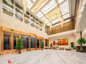 Eine geräumige Lobby mit hoher Decke, großen Fenstern und einer zentralen Sitzgelegenheit.