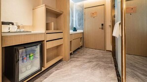 A compact hotel room with a kitchenette, a mini-fridge, a small refrigerator, and a shower area.
