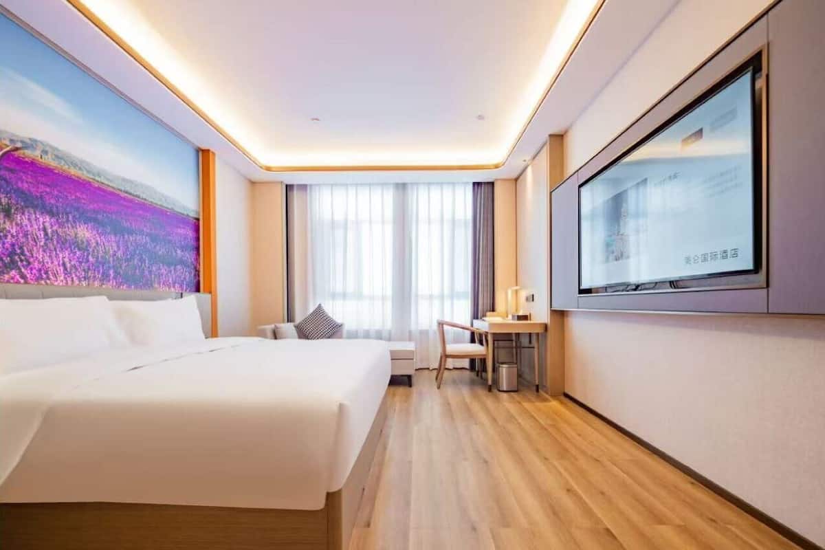 Una habitación de hotel con cama, escritorio, televisor y un ventanal grande.