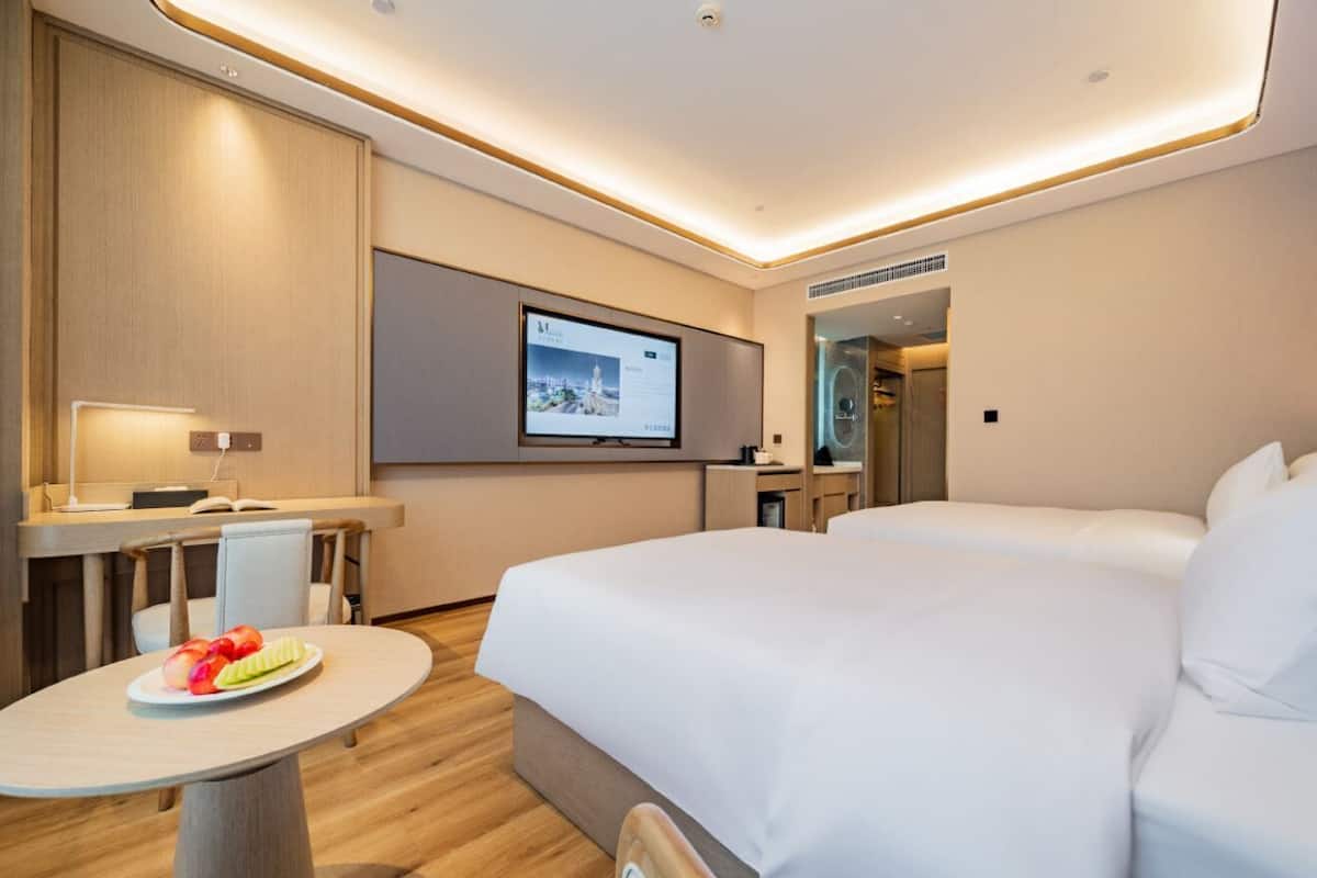 Una habitación de hotel moderna con cama, escritorio, silla, una mesita con fruta y una pantalla de televisión.